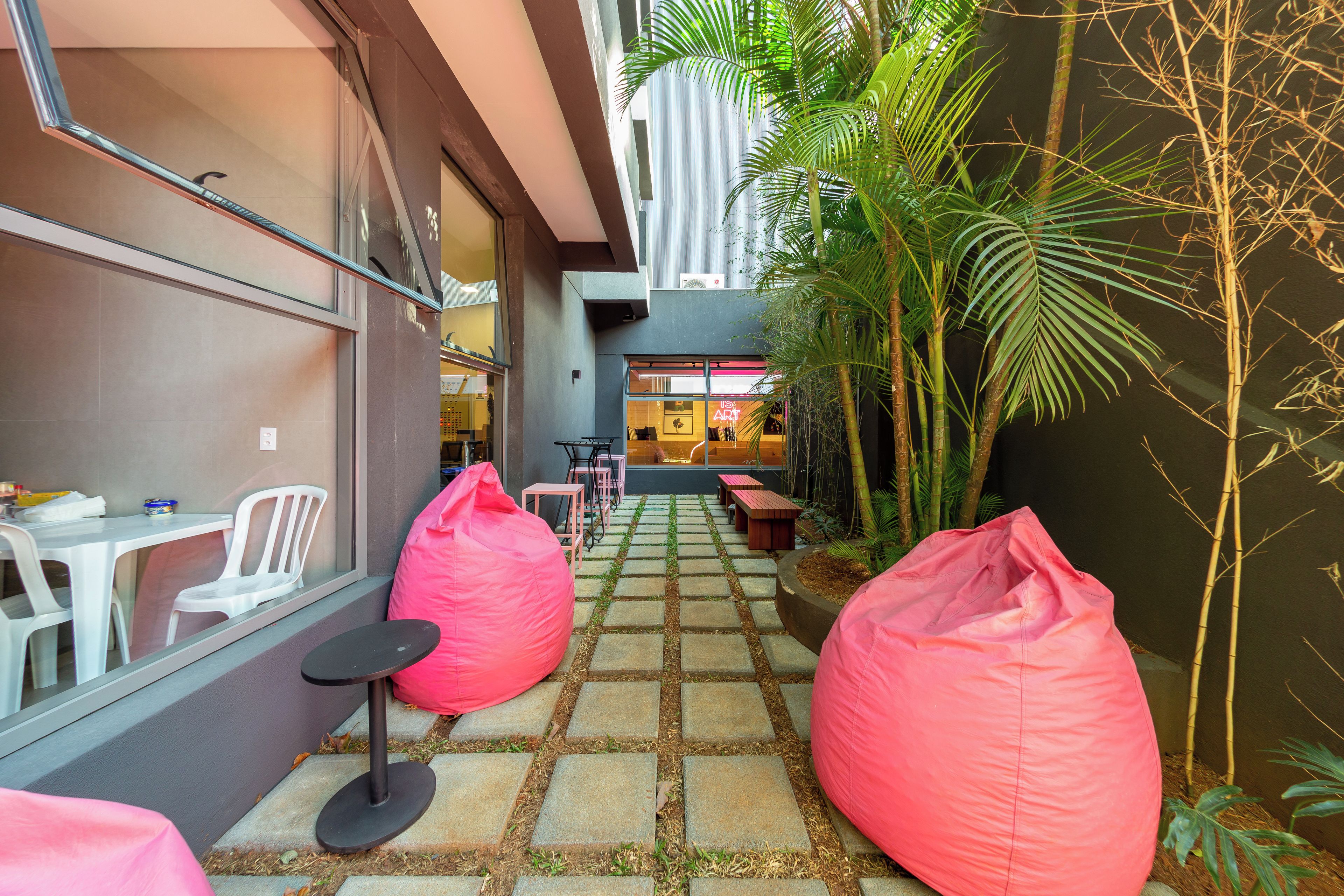 A narrow outdoor corridor with a stone-tiled floor, two pink bean bags, and a seating area with tables and chairs.