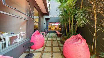 A narrow outdoor corridor with a stone-tiled floor, two pink bean bags, and a seating area with tables and chairs.