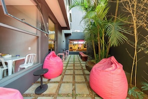 A narrow outdoor corridor with a stone-tiled floor, two pink bean bags, and a seating area with tables and chairs. - Maracatins By Bhomy (São Paulo)