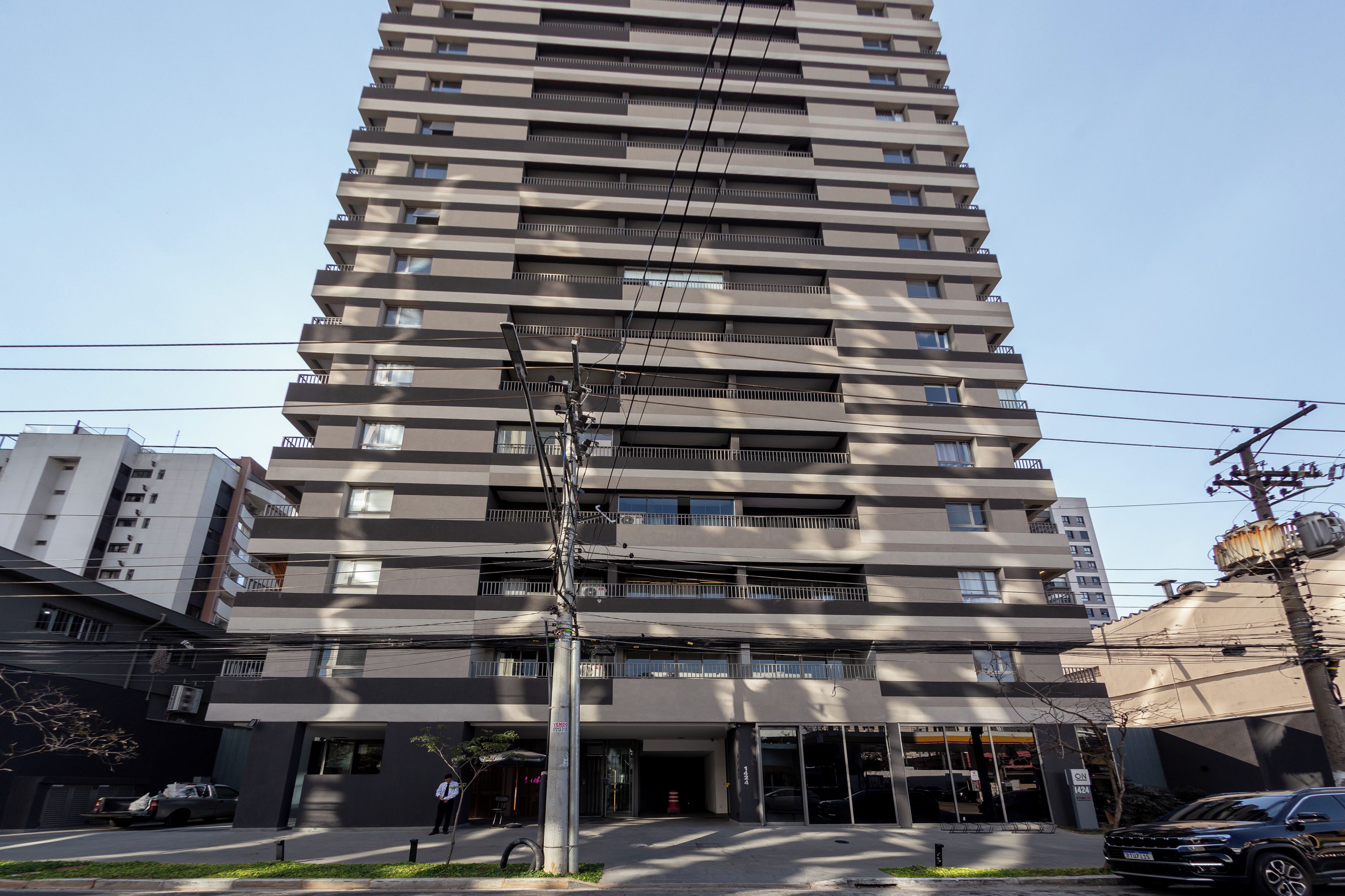 A multi-story building with a modern architectural design, featuring balconies on each floor and a ground-level entrance with a visible storefront.