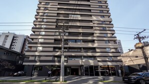 Um edifício com vários andares e design arquitetônico moderno, com varandas em cada pavimento e entrada no nível da rua com uma vitrine visível.