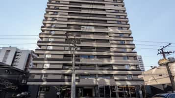 A multi-story building with a modern architectural design, featuring balconies on each floor and a ground-level entrance with a visible storefront.