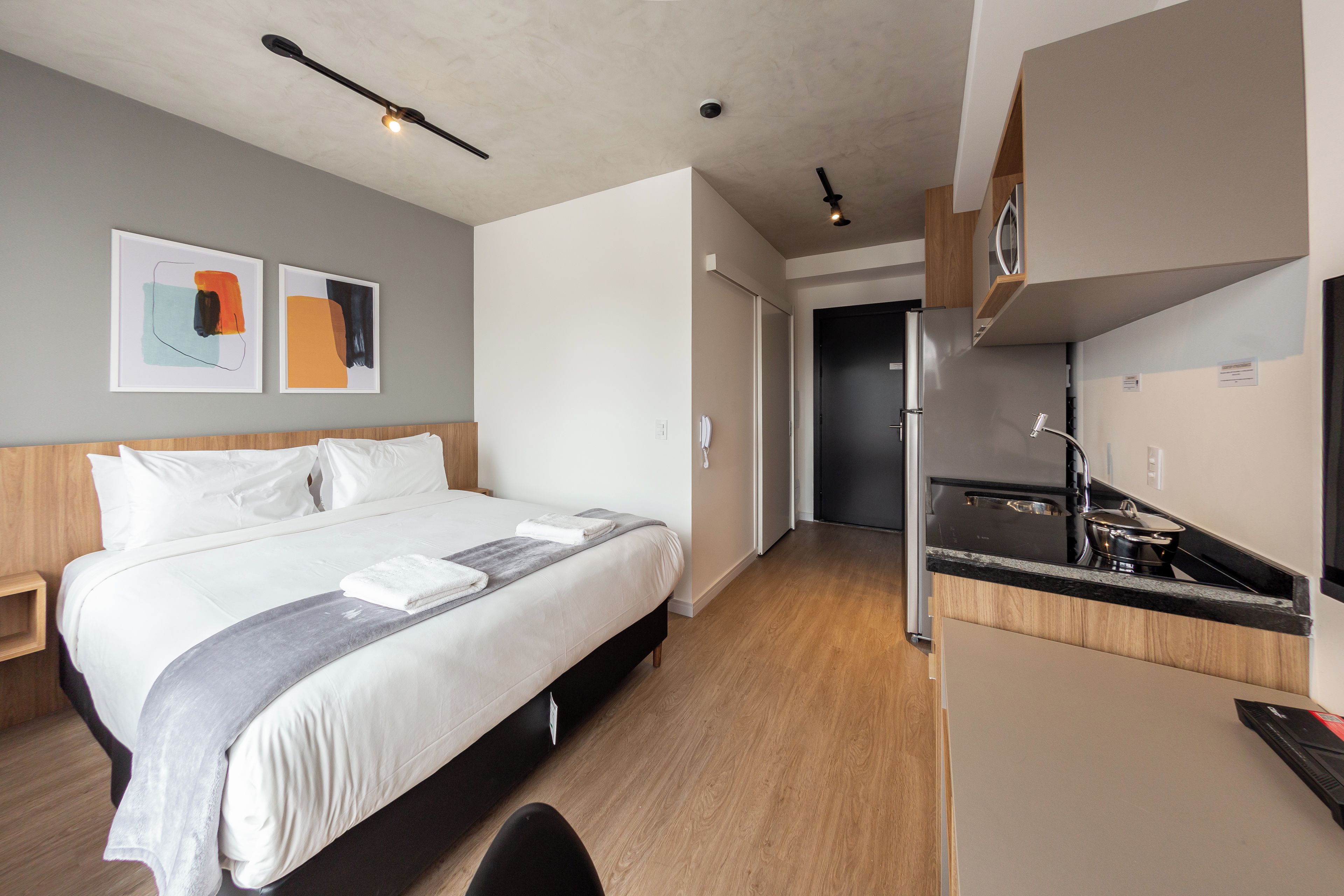 A hotel room with a bed, bedside table, and a kitchenette area.