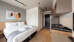 Quarto de hotel com cama, mesa de cabeceira e uma pequena cozinha.