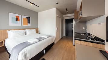 A hotel room with a bed, bedside table, and a kitchenette area.