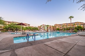 A swimming pool area with multiple pools, lounge chairs, and a building with balconies in the background.