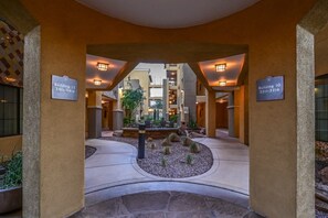 A hotel lobby with a central seating area, two building signs, and a stone fountain.