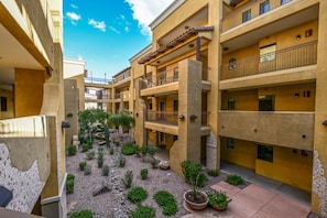 A courtyard with multiple balconies, potted plants, and a clear sky.