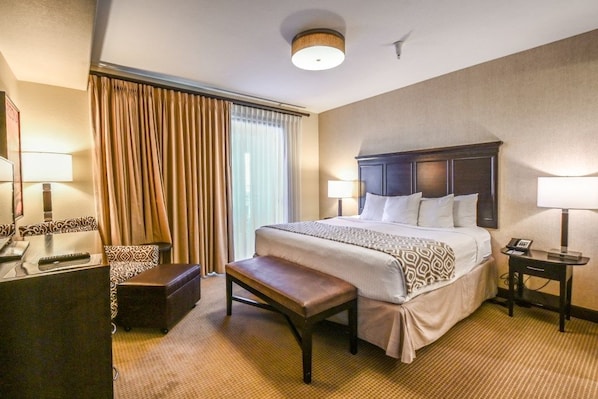 A hotel room with a large bed, a desk, a bench, and a lamp.