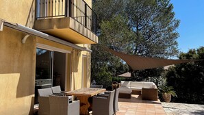 En udendørs terrasse med spisebord og fletningsmøbler, et overdækket siddeområde og en bygning med balkon.