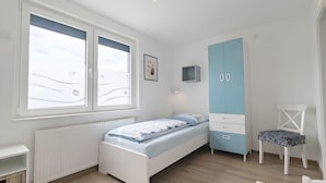 Ein Schlafzimmer mit Bett, Kleiderschrank, Stuhl, Schreibtisch und einem Fenster mit Jalousien.