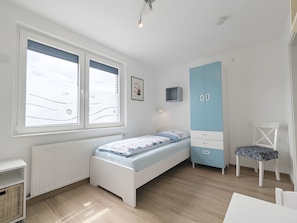 Quarto com cama, guarda-roupa, cadeira, escrivaninha e janela com persianas.