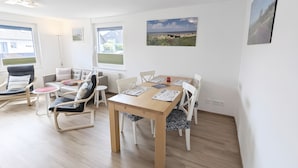 Ein helles Zimmer mit Esstisch, Stühlen, einer Couch und einem Fenster.