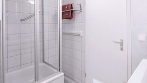 Ein modernes Badezimmer mit einer gläsernen Duschkabine, weißen Fliesenwänden und Holzboden.