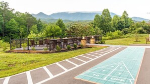 Eine Terrasse mit Sitzgelegenheiten im Freien, einem Shuffleboard-Spielfeld und Blick auf Berge.