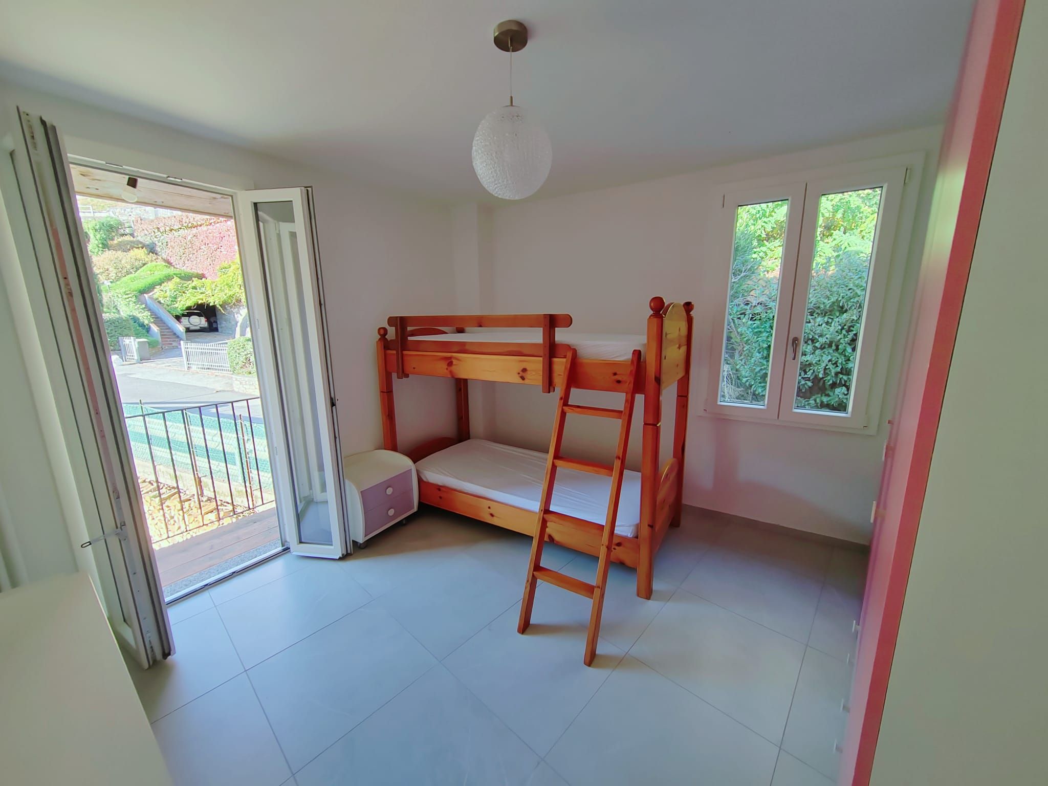 A room with a bunk bed, a ladder, a door leading to a balcony, and a window.