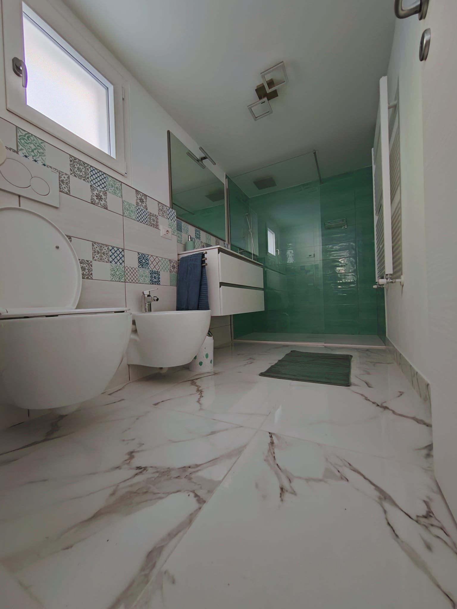 Un baño con inodoro, bidé y lavabo, un espejo y una ducha con puerta verde.