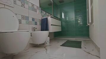 Un baño con inodoro, bidé y lavabo, un espejo y una ducha con puerta verde.