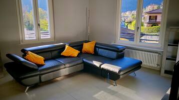 Una sala de estar moderna con un sofá seccional, dos ventanas con vistas a una zona residencial y un radiador.