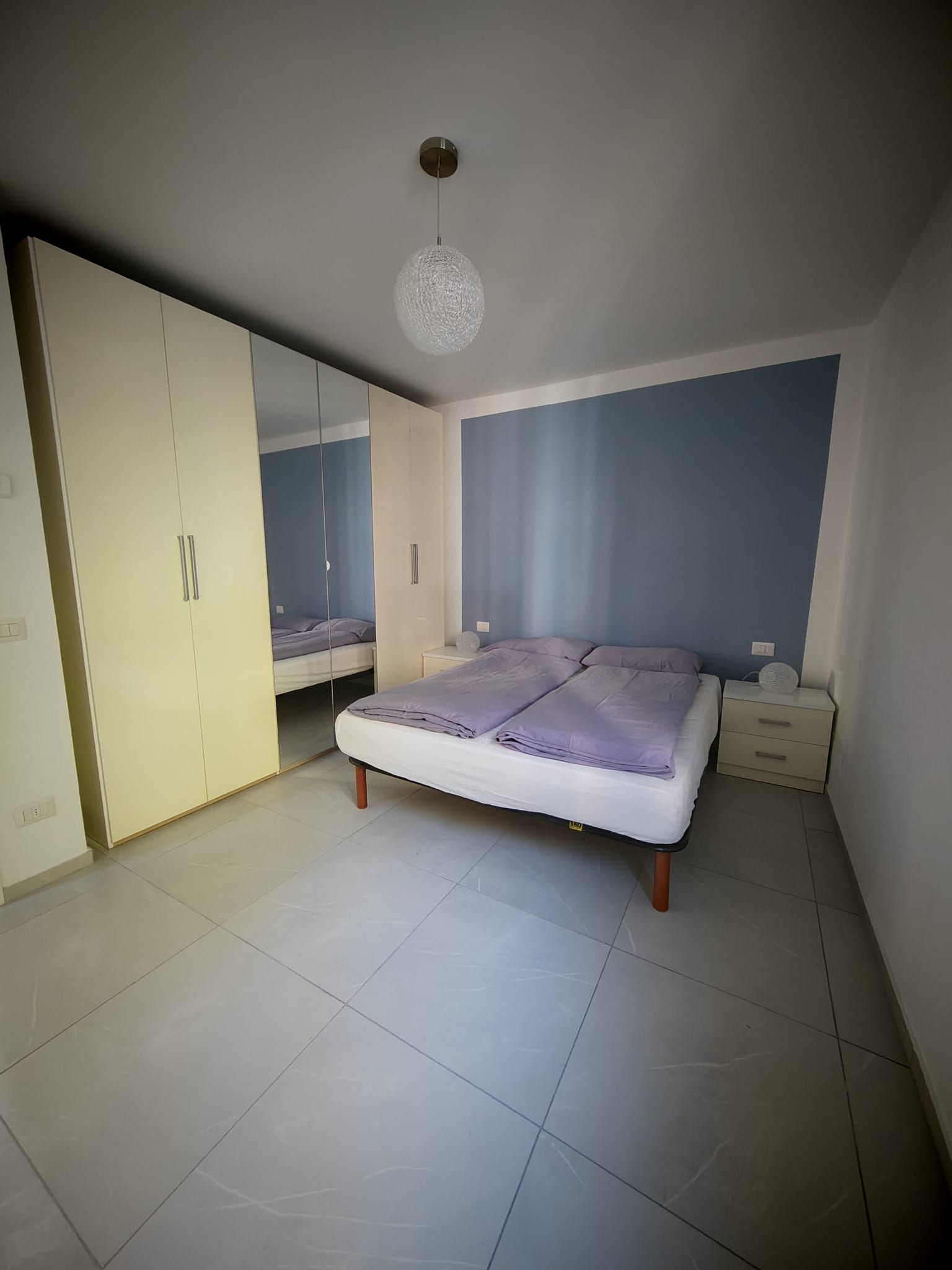 Ein Schlafzimmer mit einem Bett, einem Kleiderschrank, einem Nachttisch und einer Pendelleuchte.