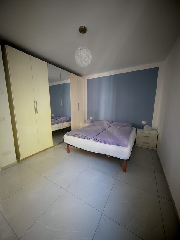 Ein Schlafzimmer mit einem Bett, einem Kleiderschrank, einem Nachttisch und einer Pendelleuchte.