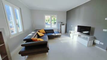 A modern living room with a sectional sofa, a flat-screen TV, and a view of a garden through large windows.