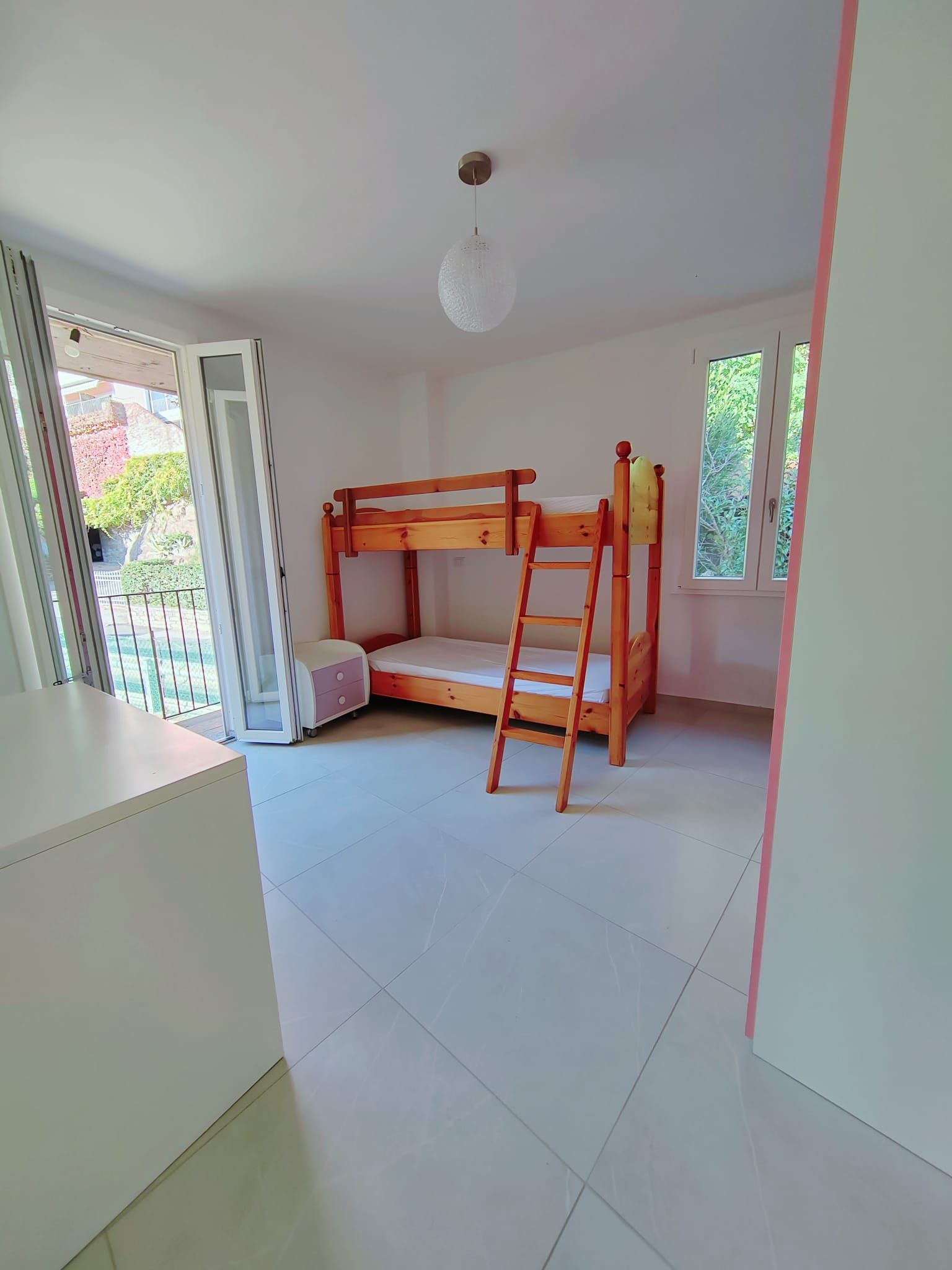 Una habitación con literas, una escalera, una mesita y una ventana.
