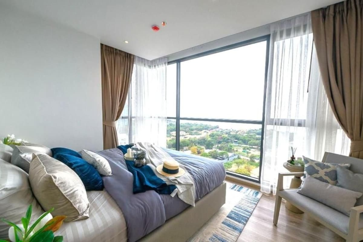 A modern bedroom with a large bed, a sofa, and a view of a cityscape through large windows.