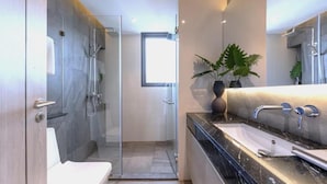 A modern bathroom with a glass shower enclosure, a white toilet, a black marble sink, and a potted plant. - Andromeda Condominium Pattaya (Muang Pattaya)