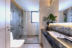 A modern bathroom with a glass shower enclosure, a white toilet, a black marble sink, and a potted plant. - Andromeda Condominium Pattaya (Muang Pattaya)