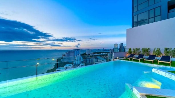 A rooftop infinity pool with a city view, lounge chairs, and a modern building structure. - Andromeda Condominium Pattaya (Muang Pattaya)