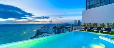 A rooftop infinity pool with a city view, lounge chairs, and a modern building structure.