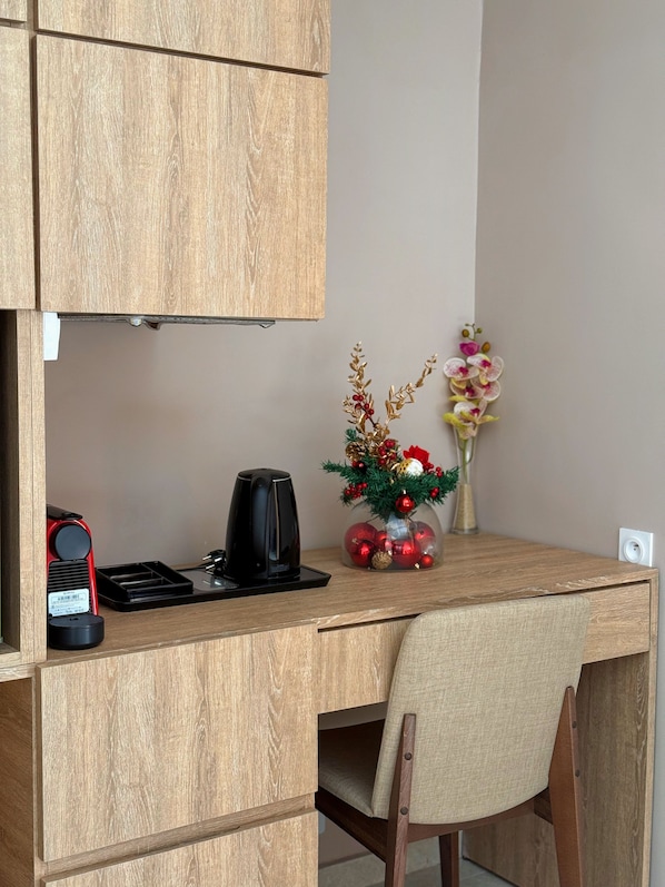 A wooden desk with a black coffee maker, a red and black device, and a vase with flowers and ornaments.