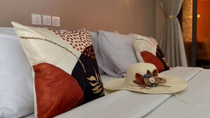 Ein ordentlich bezogenes Bett mit gemusterten Kissen, einem dekorativen Hut und einer Wandleuchte.