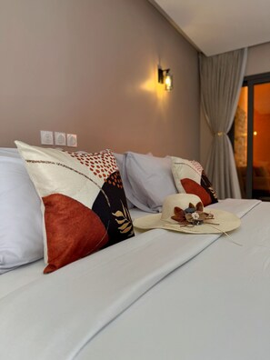 Un letto rifatto con cuscini decorati, un cappello ornamentale e un portalampada a parete.