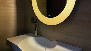 Ein modernes Badezimmer mit einem weißen Waschbecken, einem runden Spiegel mit Beleuchtung und einer dunklen Wand.