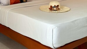 Ein ordentlich bezogenes Bett mit weißer Bettwäsche und dekorativen Kissen, eine Wandleuchte und ein kleiner Hut auf dem Bett.