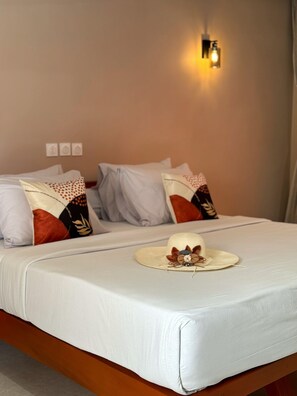 Un letto rifatto con biancheria bianca e cuscini decorativi, un lampadario a parete e un cappello appoggiato sul letto.