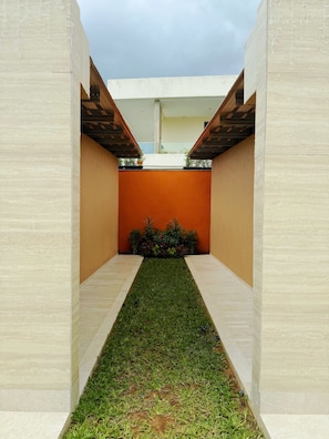 A narrow pathway leading to a building with a flat roof and a small garden area.