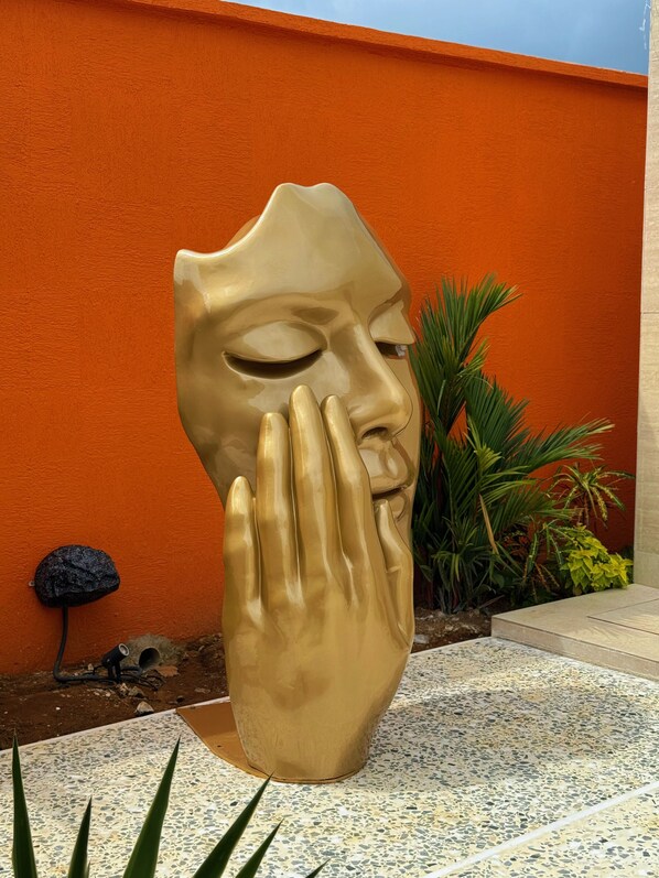 Una scultura raffigura una mano in un giardino con pareti arancioni e piante verdi.