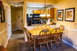 A dining area with a wooden table and chairs, a kitchen in the background, and framed artwork on the wall. - Pigeon Forge | Smoky Mountain Villa | Spa + Pool (Pigeon Forge)