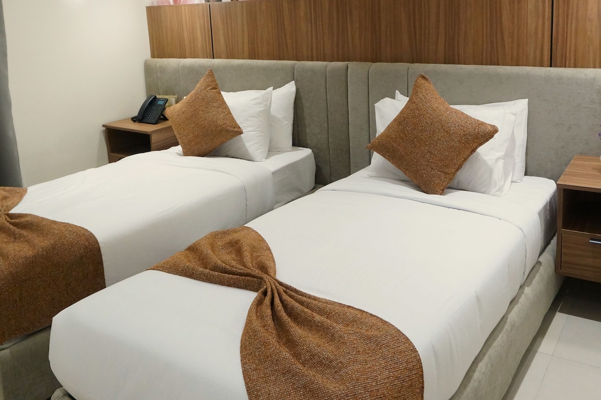 Ein Hotelzimmer mit zwei Betten, einem Nachttisch mit Telefon und einer Wand mit Blättermuster.
