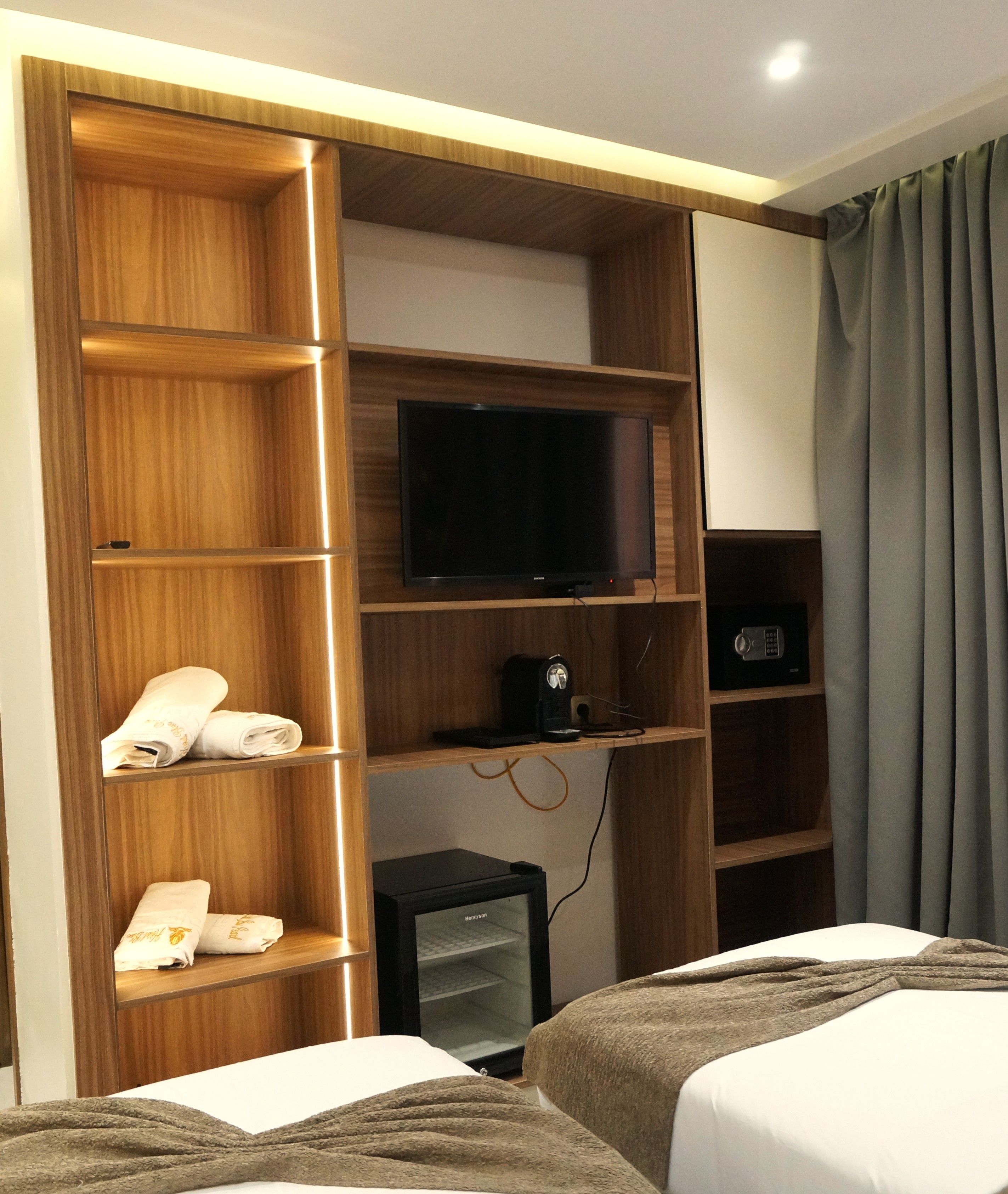 Habitación de hotel con armario de madera, televisor de pantalla plana, cafetera y cama con manta.