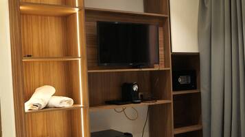 Habitación de hotel con armario de madera, televisor de pantalla plana, cafetera y cama con manta.