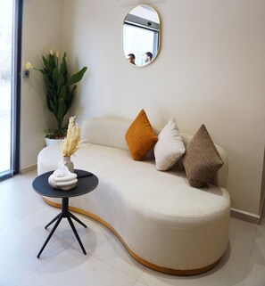 Ein modernes Wohnzimmer mit einer gebogenen Couch, einem runden Spiegel und einem kleinen, runden Tisch mit einer Vase.