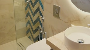 Um banheiro moderno com box de vidro, vaso sanitário branco e toucador com duas pias.