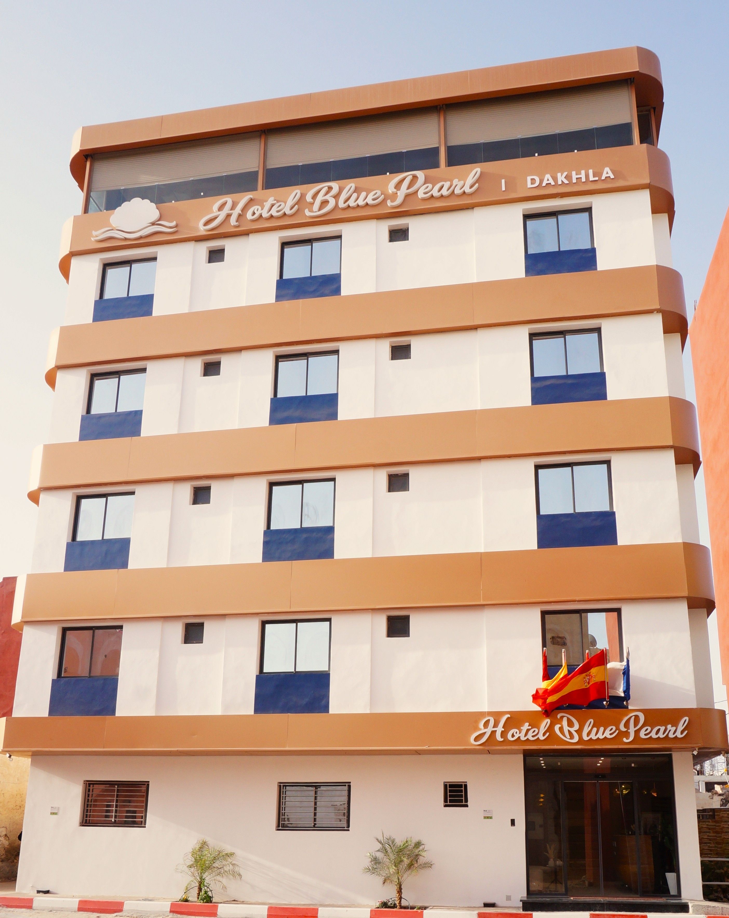 A multi-story hotel building with a sign reading 'Hotel Blue Pearl' and 'Dakhla' indicating its location.