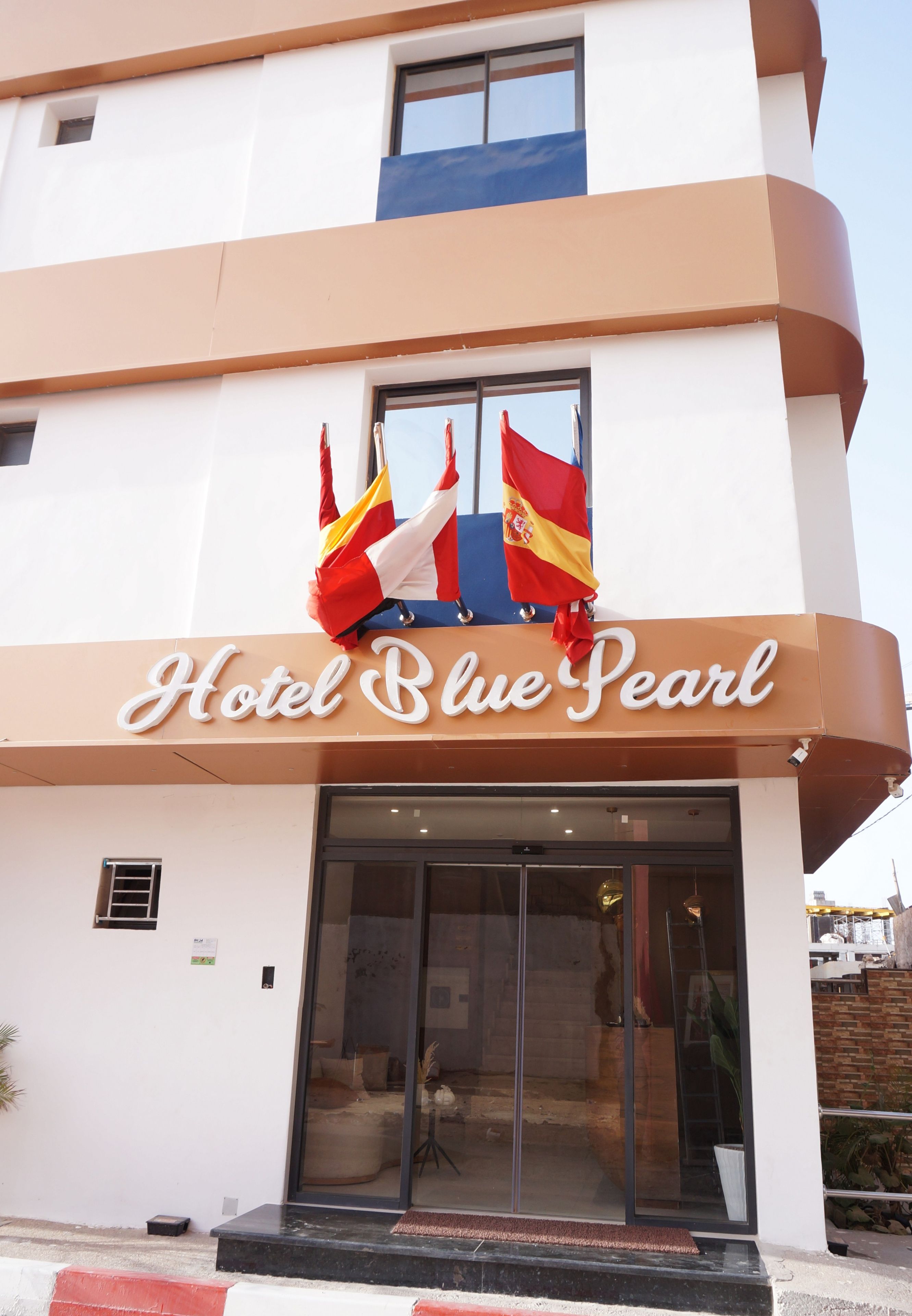 Entrada d'hotel amb un rètol que diu 'Hotel Blue Pearl' i dues banderes sobre l'entrada.