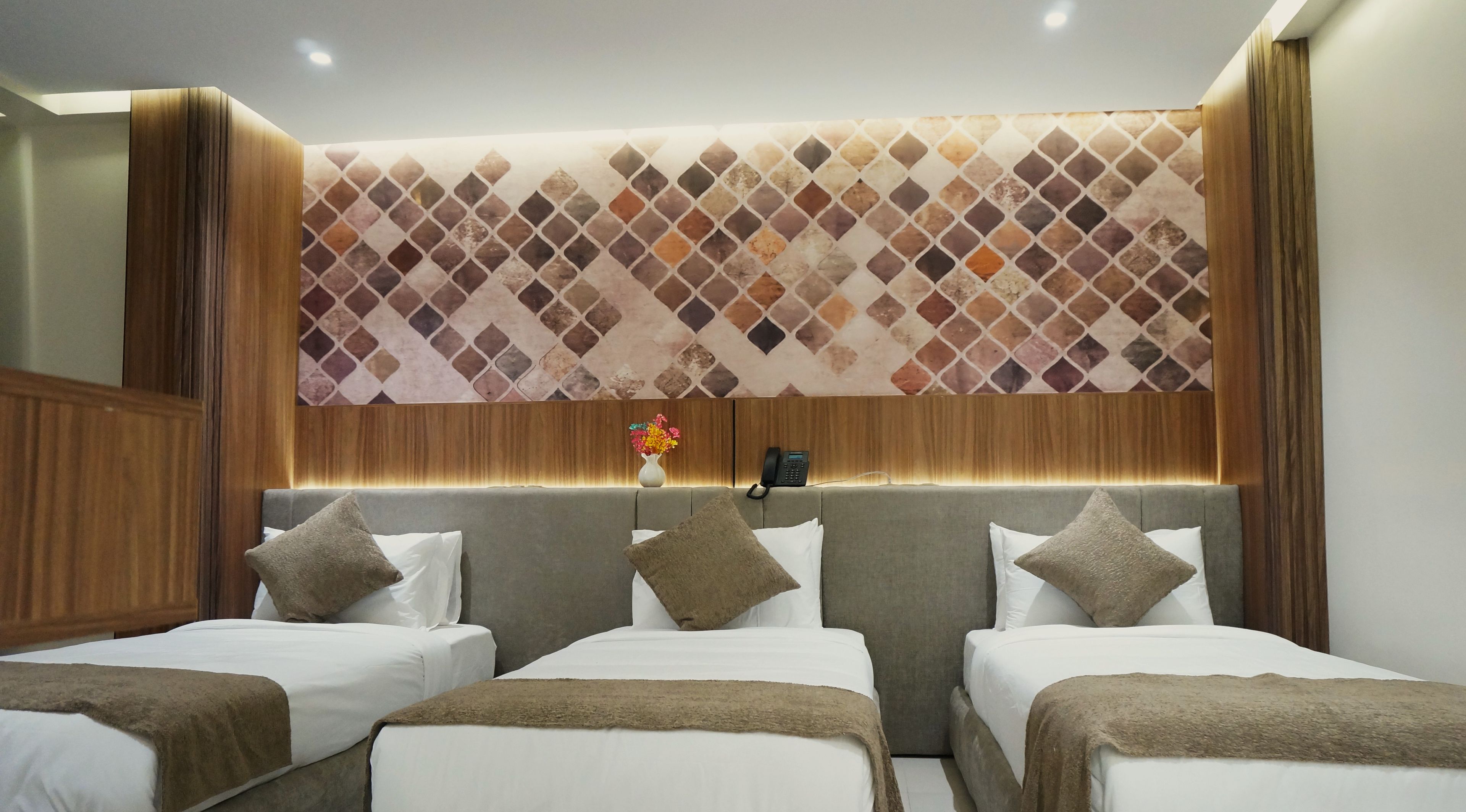 A hotel room with a modern design, featuring a large bed with two pillows and a headboard with a patterned design.