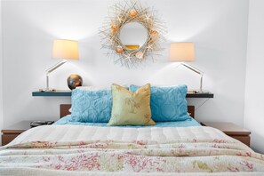 A bedroom with a bed, two bedside tables, two lamps, a decorative mirror, and a wall-mounted wreath. - 4BR Beach Cottage Pool Walk to Beach (St. Augustine)